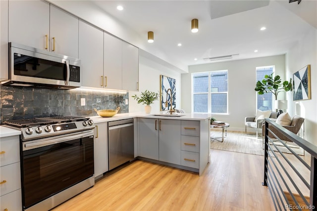 kitchen with stainless steel appliances, a peninsula, gray cabinets, light wood finished floors, and light countertops