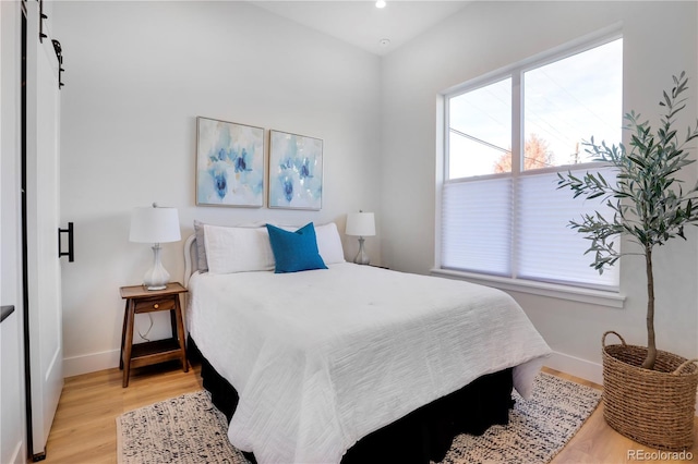 bedroom featuring baseboards, light wood-type flooring, recessed lighting, and a barn door