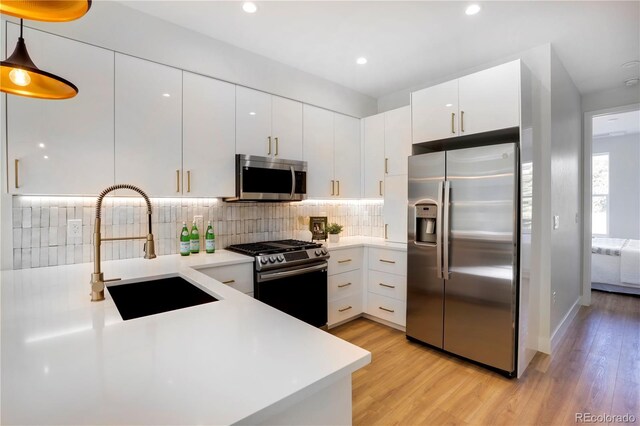 kitchen featuring appliances with stainless steel finishes, a sink, light wood-style flooring, white cabinets, and light countertops