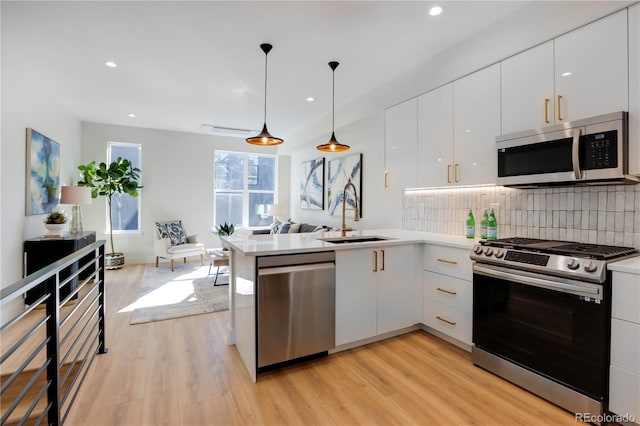 kitchen with stainless steel appliances, a sink, white cabinets, light wood finished floors, and recessed lighting