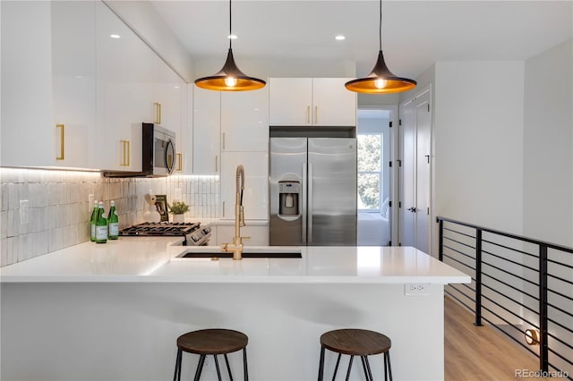 kitchen with stainless steel appliances, a peninsula, a breakfast bar area, white cabinetry, and decorative light fixtures