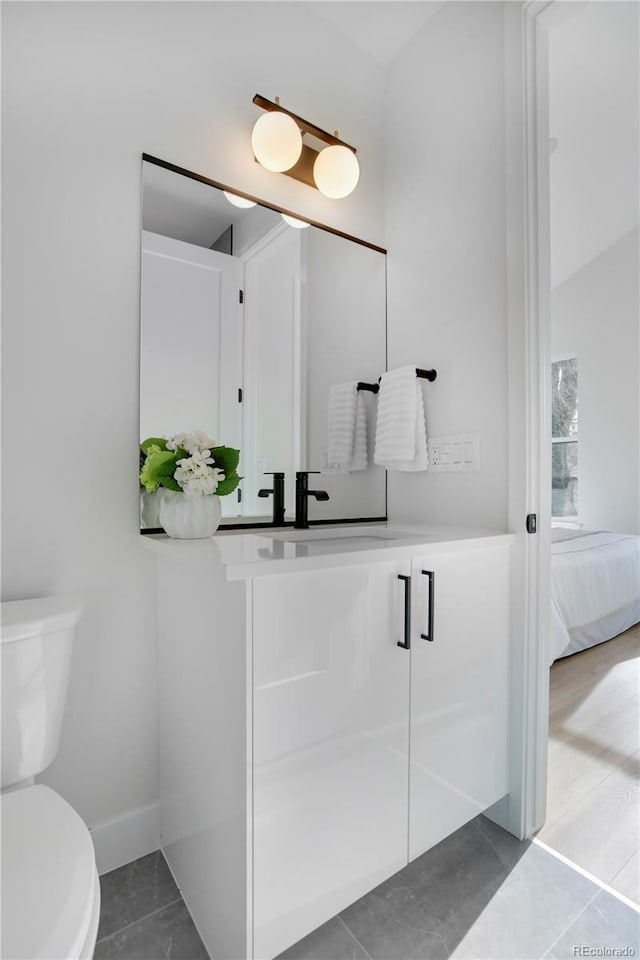 ensuite bathroom with toilet, vanity, baseboards, and tile patterned flooring