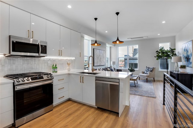 kitchen featuring appliances with stainless steel finishes, a sink, open floor plan, modern cabinets, and a peninsula