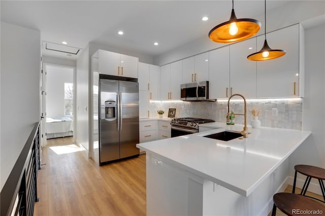 kitchen featuring appliances with stainless steel finishes, a sink, light wood-style flooring, a peninsula, and light countertops