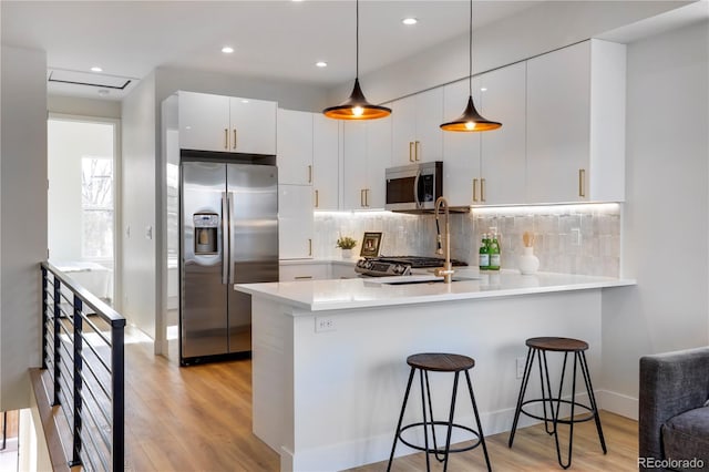 kitchen featuring stainless steel appliances, a peninsula, light wood finished floors, backsplash, and recessed lighting
