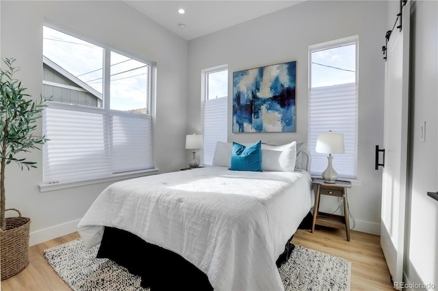 bedroom with a barn door, multiple windows, light wood finished floors, and baseboards