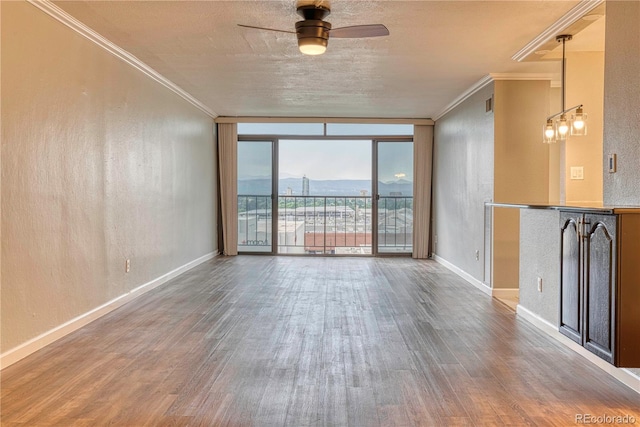 spare room with hardwood / wood-style flooring, ornamental molding, expansive windows, and ceiling fan