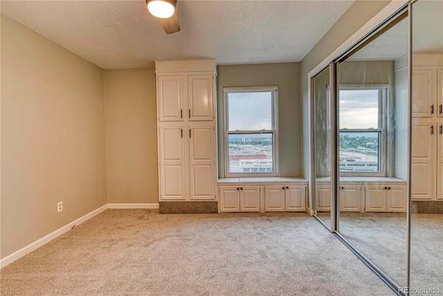 unfurnished bedroom featuring ceiling fan, light colored carpet, a closet, and a textured ceiling