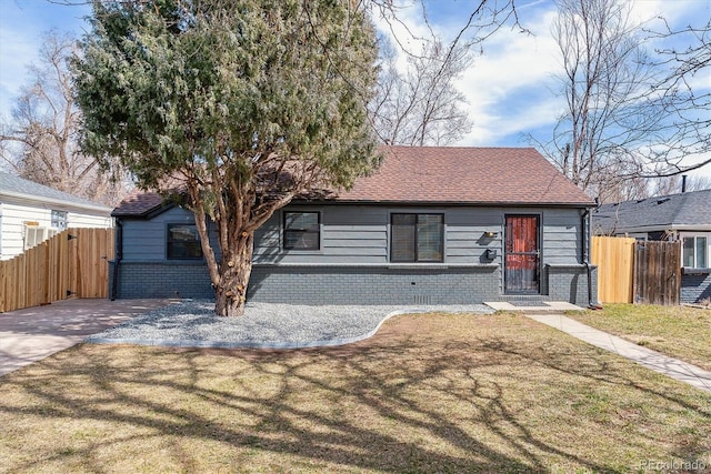 view of front of property featuring brick siding, roof with shingles, a front lawn, and fence