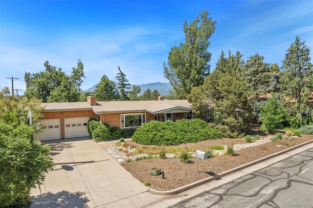 1601 Columbine Pl, Colorado Springs, CO 80907 - ranch-style house featuring an attached garage, a chimney, concrete driveway, brick siding, and a mountain view