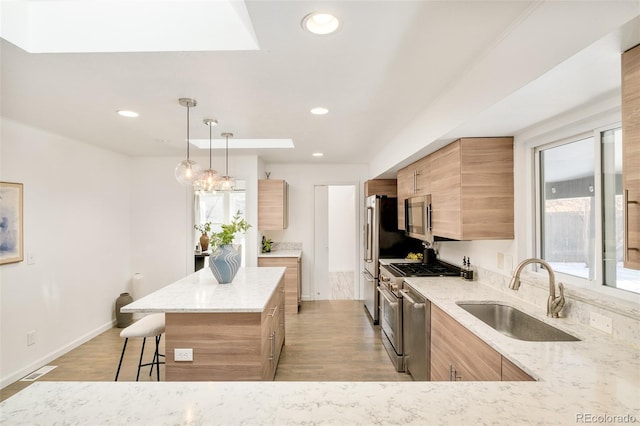 kitchen with stainless steel appliances, hanging light fixtures, a kitchen island, a sink, and light stone countertops