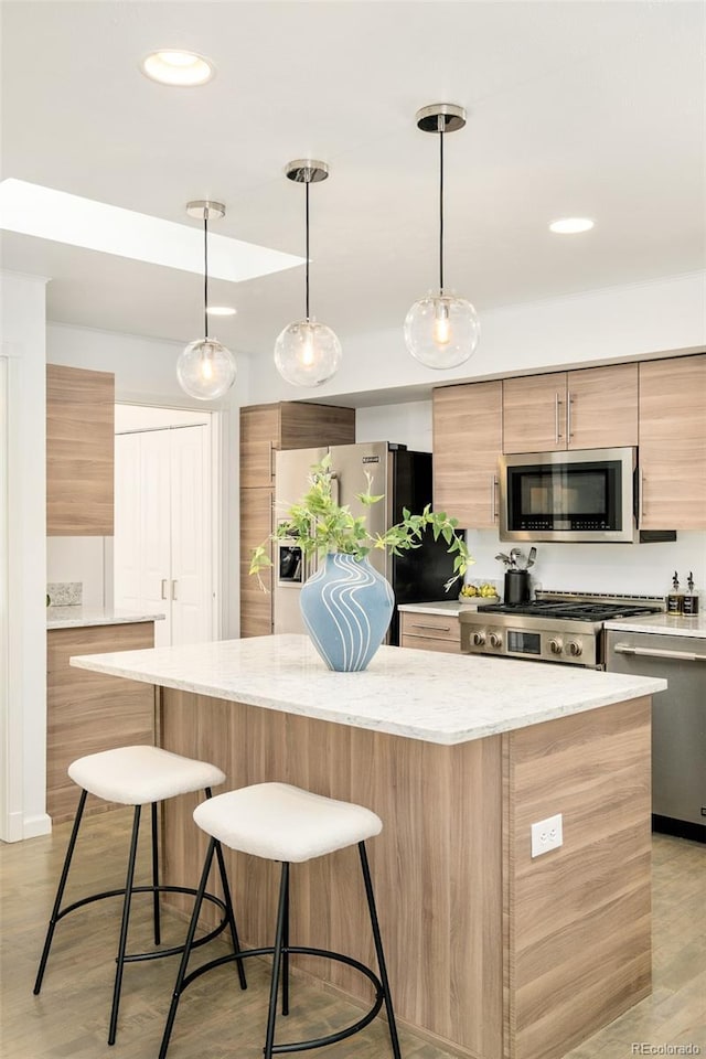 kitchen featuring modern cabinets, a kitchen island, appliances with stainless steel finishes, light stone counters, and decorative light fixtures