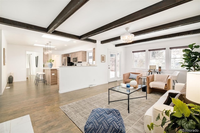 living room with an inviting chandelier, beam ceiling, baseboards, and light wood-style floors