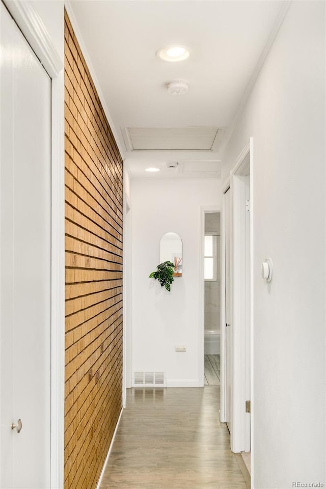 corridor featuring brick wall, wood finished floors, and visible vents