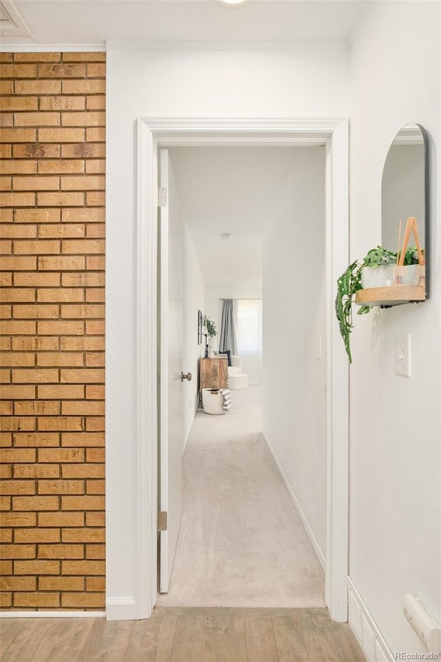 corridor with baseboards, brick wall, light carpet, and light wood-style floors