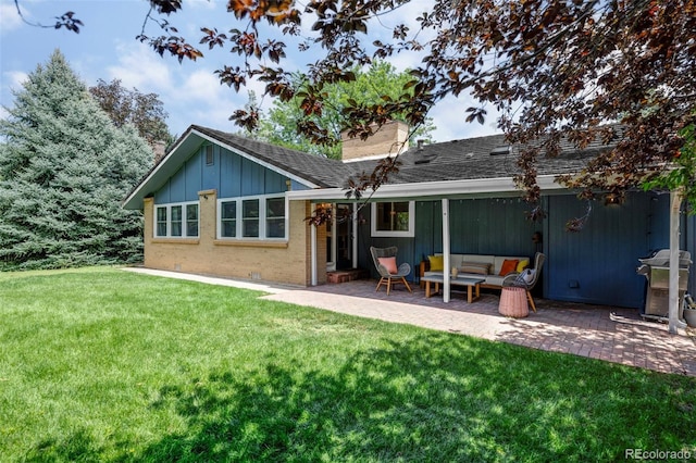 rear view of property with brick siding, a yard, a chimney, a patio, and board and batten siding