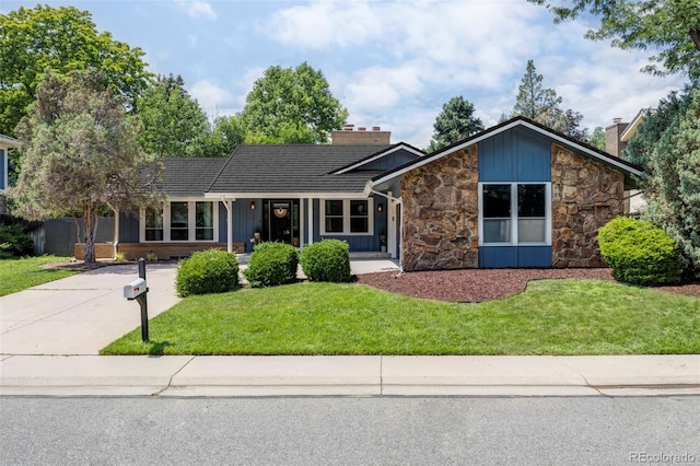 mid-century modern home with stone siding, a chimney, board and batten siding, and a front yard