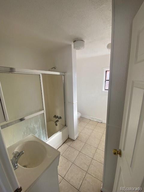 full bathroom with shower / bath combination with glass door, tile patterned flooring, vanity, a textured ceiling, and toilet