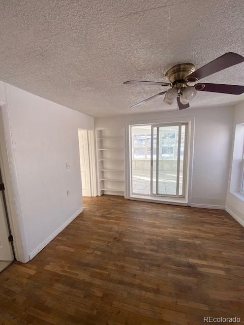 spare room with built in shelves, ceiling fan, dark hardwood / wood-style floors, and a textured ceiling