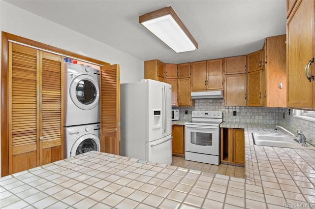 561 Quartz Cir, Bailey, CO 80421 - kitchen featuring white appliances, stacked washer and clothes dryer, tile countertops, under cabinet range hood, and tasteful backsplash