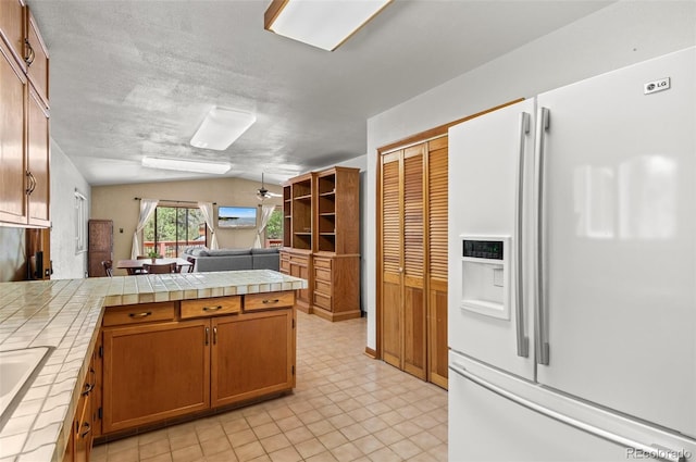 561 Quartz Cir, Bailey, CO 80421 - kitchen with white refrigerator with ice dispenser, tile counters, a peninsula, vaulted ceiling, and open floor plan