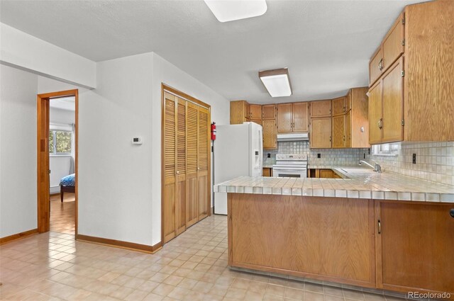 561 Quartz Cir, Bailey, CO 80421 - kitchen with white appliances, under cabinet range hood, backsplash, a peninsula, and brown cabinets