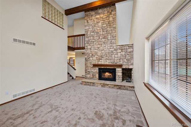 unfurnished living room featuring a high ceiling, carpet, a fireplace, and beamed ceiling