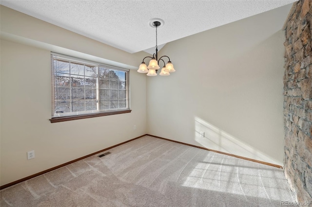 carpeted empty room featuring a chandelier and a textured ceiling