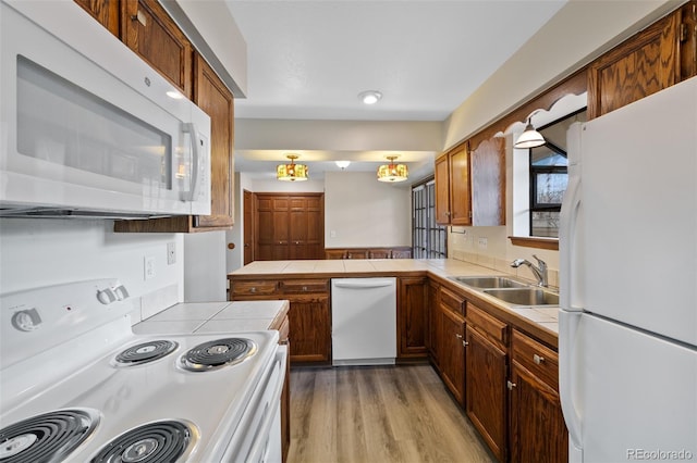 kitchen with sink, white appliances, tile countertops, and light wood-type flooring