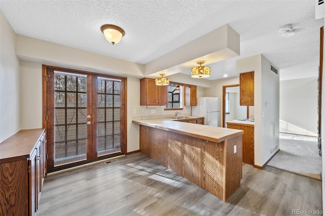 kitchen featuring french doors, tile countertops, kitchen peninsula, white fridge, and light hardwood / wood-style floors