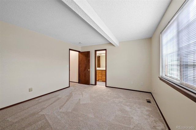 unfurnished bedroom featuring beam ceiling, light carpet, a textured ceiling, and ensuite bath