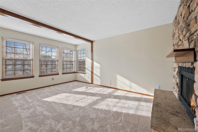 unfurnished living room featuring beamed ceiling, light colored carpet, a fireplace, and a textured ceiling