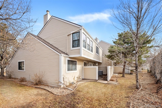 rear view of property with central AC unit and a lawn