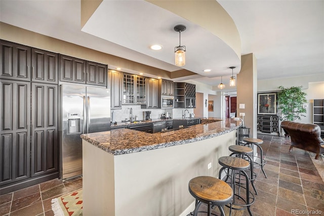 kitchen featuring sink, a breakfast bar area, dark stone counters, hanging light fixtures, and built in appliances