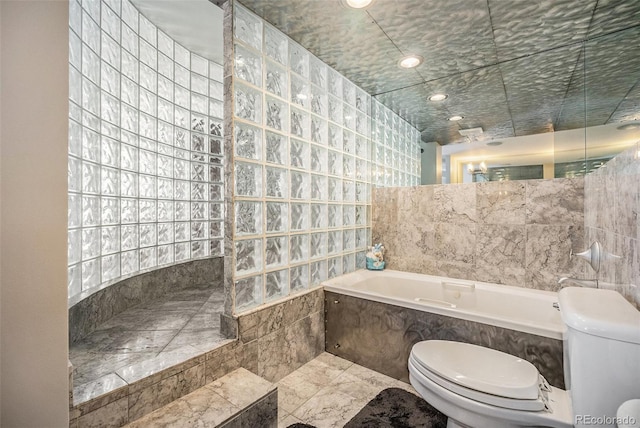 bathroom with tile walls, tiled bath, and toilet