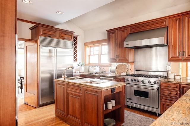 kitchen with lofted ceiling, wall chimney range hood, light hardwood / wood-style flooring, high quality appliances, and light stone counters