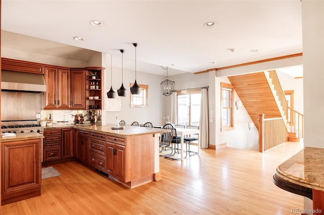 kitchen featuring a notable chandelier, decorative light fixtures, kitchen peninsula, wall chimney exhaust hood, and light wood-type flooring