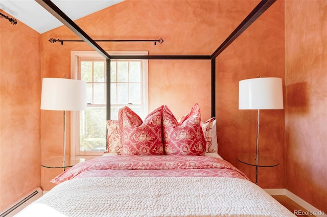 bedroom with vaulted ceiling, wood-type flooring, and a baseboard heating unit