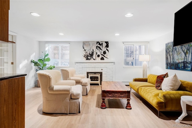 living room with a baseboard radiator, a brick fireplace, a wealth of natural light, and light hardwood / wood-style flooring