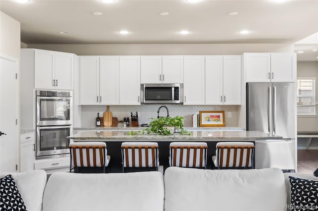 4778 Ravencrest Pl, Castle Rock, CO 80108 - kitchen with appliances with stainless steel finishes, white cabinetry, light stone countertops, a center island with sink, and tasteful backsplash