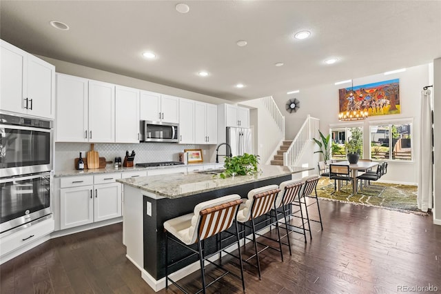4778 Ravencrest Pl, Castle Rock, CO 80108 - kitchen with appliances with stainless steel finishes, a kitchen breakfast bar, dark wood-type flooring, backsplash, and a center island with sink