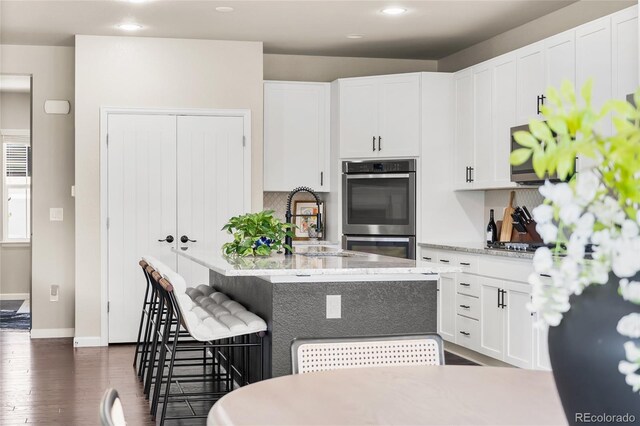 4778 Ravencrest Pl, Castle Rock, CO 80108 - kitchen with appliances with stainless steel finishes, dark wood-style flooring, a kitchen breakfast bar, white cabinetry, and recessed lighting