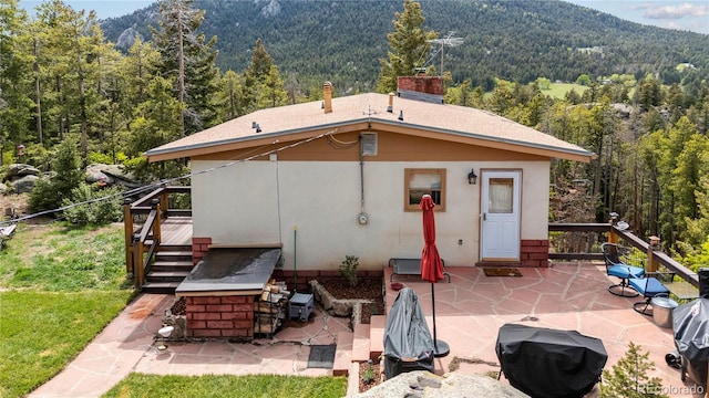 8701 Majestic View Dr, Conifer, CO 80433 - rear view of house featuring a forest view, a patio area, stucco siding, a mountain view, and a chimney