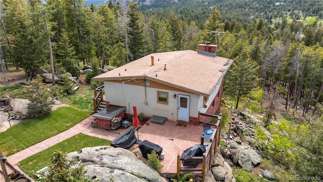 8701 Majestic View Dr, Conifer, CO 80433 - back of property with a view of trees, a patio, a chimney, stucco siding, and roof with shingles