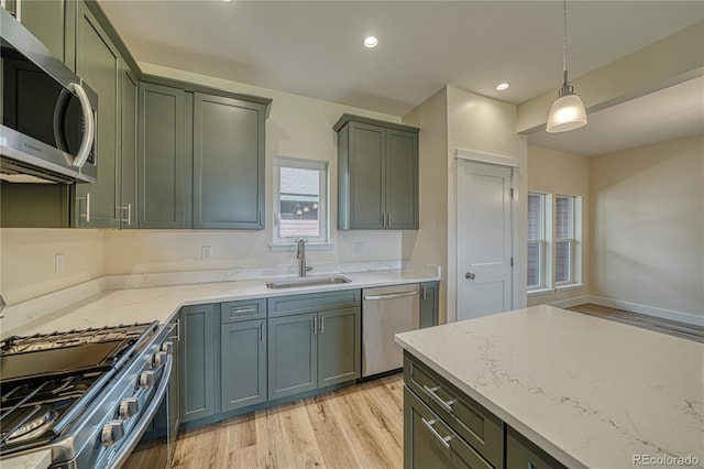 kitchen featuring light stone countertops, sink, hanging light fixtures, stainless steel appliances, and light wood-type flooring