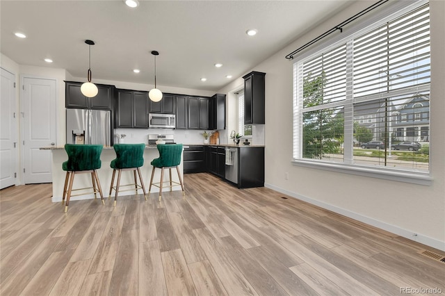 9307 Inca Dove Cir, Littleton, CO 80125 - kitchen featuring appliances with stainless steel finishes, a kitchen island, light wood-style floors, light countertops, and a kitchen bar