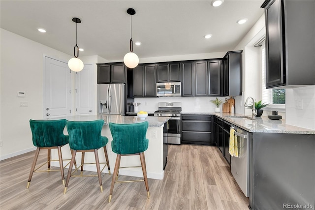 9307 Inca Dove Cir, Littleton, CO 80125 - kitchen with appliances with stainless steel finishes, light wood-type flooring, light stone counters, a kitchen island, and recessed lighting