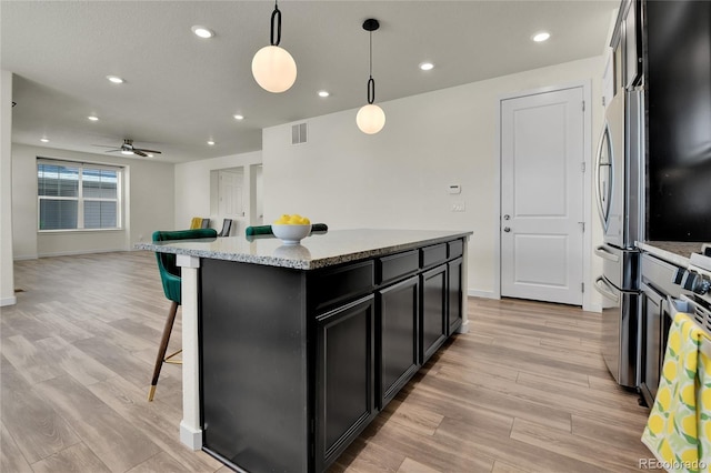 9307 Inca Dove Cir, Littleton, CO 80125 - kitchen featuring dark cabinets, open floor plan, ceiling fan, a kitchen breakfast bar, and light wood finished floors