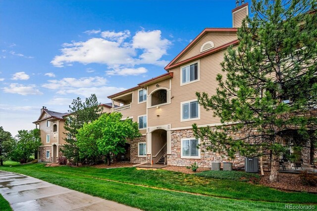 8520 S Holland Ln Unit 102, Littleton, CO 80128 - view of front of house featuring stone siding, central air condition unit, a front yard, and a chimney