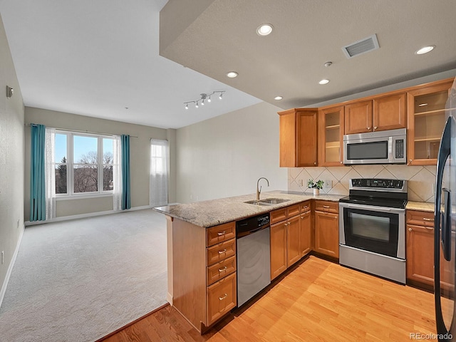 kitchen featuring sink, backsplash, stainless steel appliances, light stone countertops, and kitchen peninsula